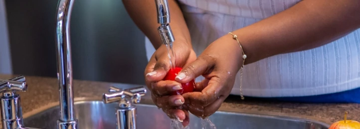 Hands washing a red apple under running water in a kitchen sink.