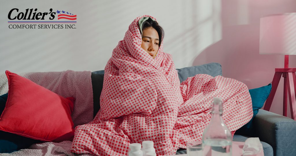 A miserable woman with a cold wrapped up in a blanket on her sofa.